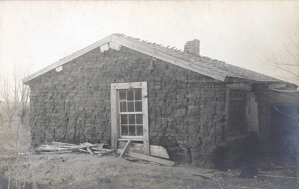 An old black-and-white photo of a Nebraska sod house with a shingled roof and one window